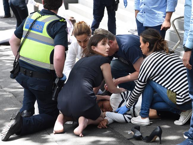 A woman in a smart dress and bare feet cradles an injured woman in the recovery position. Picture: Tony Gough