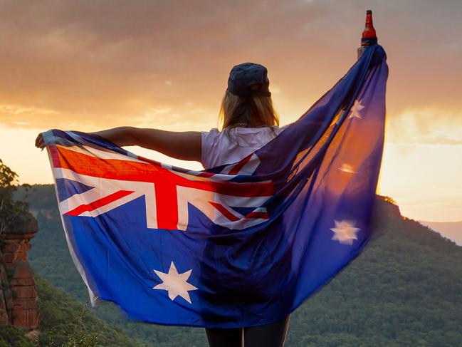 Patriotic woman holding Australian flag in Blue Mountains Australia.  Celebrate Australia Day, Sports supporter, tourism, Australian travel, Aussie Pride themes.  Selective focus to woman only.  Flag shows some motion from wind.