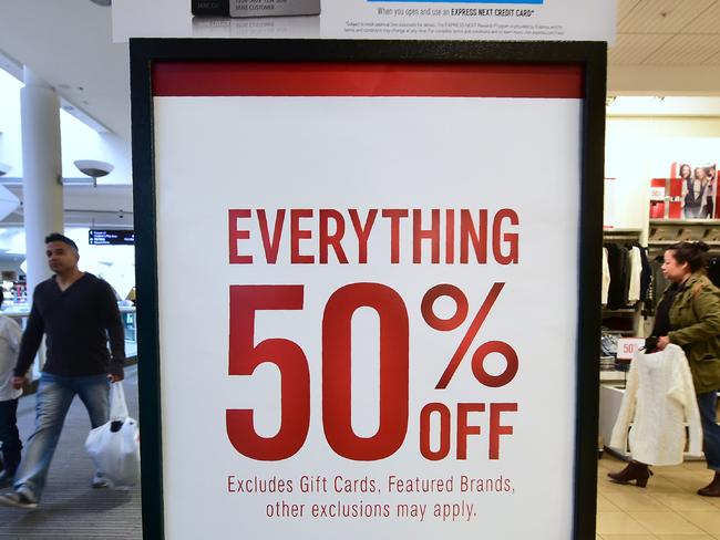 Christmas week shoppers walk past signs offering sales at a Montebello shopping mall in Montebello, California on December 22, 2016.  Shopping the week before Christmas can pay off as The National Retail Federation says they expect retailers will again be competitive on value and price in the final days.  / AFP PHOTO / Frederic J. BROWN