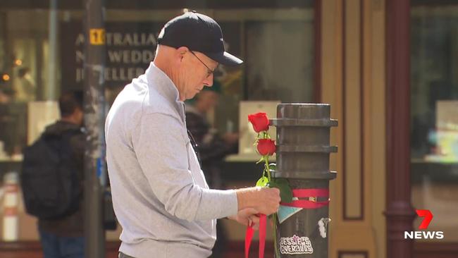 A devastated husband leaves flowers at the scene of the bus crash that killed his wife as they were crossing Grenfell Street in the CBD. Picture: 7NEWS