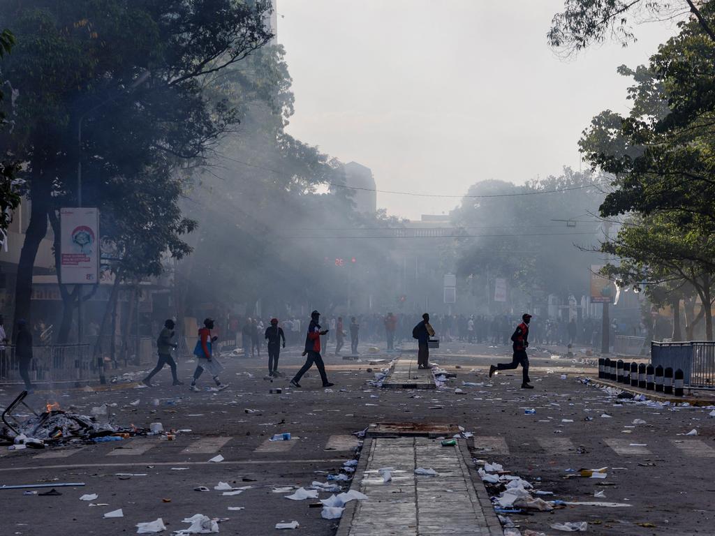 People cross a street with strewn debris in the aftermath of clashes between protesters and riot police near Nairobi’s Parliament buildings.