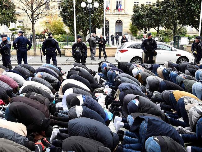 French riot police officers stand next to Muslims praying in the street during a protest in front of the city hall of Clichy, near Paris, on March 24, 2017, after an unauthorised place of worship was closed by local authorities.   / AFP PHOTO / BERTRAND GUAY