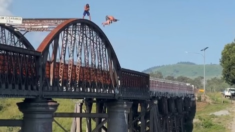 A still from the video of young men doing multiple somersaults from the top of the arch of Queenslandâ€™s oldest bridge at least 30m above the water has had almost 100,000 views and plenty of criticism.