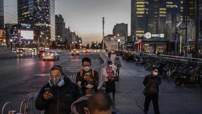 Beijing commuters wear protective masks as they line up in a staggered formation while waiting for a bus.