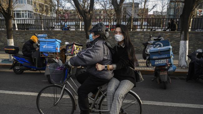 Chinese commuters wear protective masks as they ride on a bike at the end of the work day on March 20 in Beijing, where life is reportedly returning to normal.