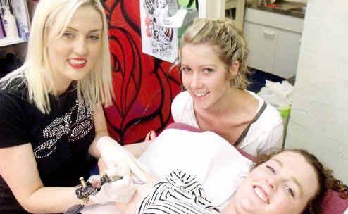 Byron Bay tattooist Tahnee Richards (left) adds a little permanence to Schoolies Week for Emily Cooper-Watts (right) and Renee Newall, both from Ballarat in Victoria. Picture: Dominic Feain