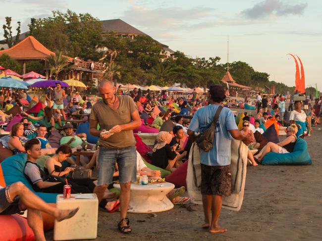 Kuta, Indonesia - February 19, 2016: A large crowd of tourists, Indonesian and foreigners, enjoy the sunset at a beach bar on Kuta beach in Seminyak, Bali.