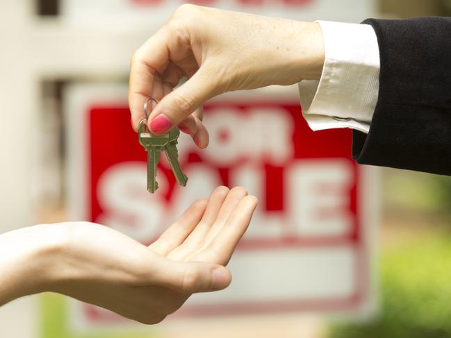 iStock photo of agent handing over keys in front of a for sale / sold sign. For On the Pulse column in Cairns Post weekend real estate liftout.