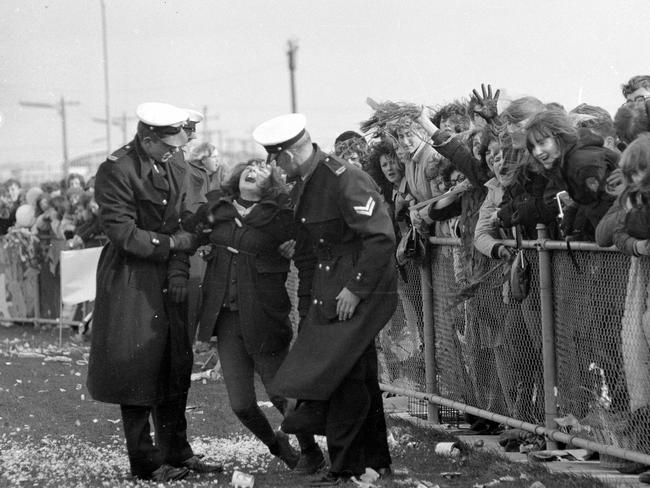 A woman, overcome with excitement at The Beatles arrival, is attended to by police at Essendon Airport. Picture: HWT Library