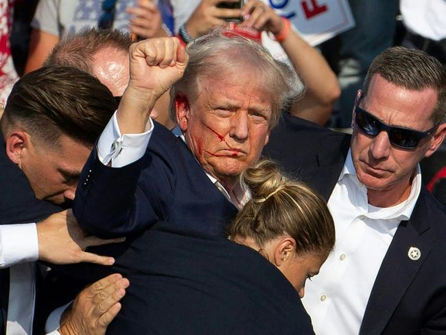 -- AFP PICTURES OF THE YEAR 2024 --  Republican Presidential candidate Donald Trump is seen with blood on his face surrounded by secret service agents as he is taken off the stage at a campaign event at Butler Farm Show Inc., in Butler, Pennsylvania, on July 13, 2024.. Donald Trump was hit in the ear in an apparent assassination attempt by a gunman at the campaign rally in a chaotic and shocking incident that will fuel fears of instability ahead of the 2024 US presidential election. The 78-year-old former president was rushed off stage with blood smeared across his face after the shooting while the gunman and a bystander were killed and two spectators critically injured. (Photo by Rebecca DROKE / AFP) / AFP PICTURES OF THE YEAR 2024