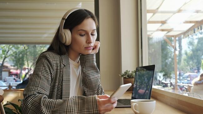 Portrait of young beautiful woman dressed in smart casual style sitting in a coffee shop with her laptop and checking her phone. Remote work concept. Close up, copy space, background.