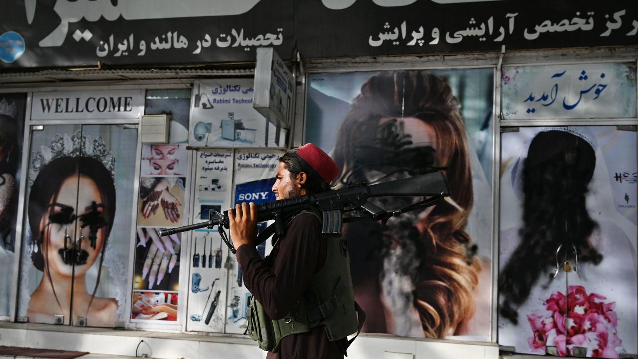 A Taliban fighter walks past a beauty salon with images of women defaced using spray paint in Kabul. Picture: Wakil Kohsar/AFP
