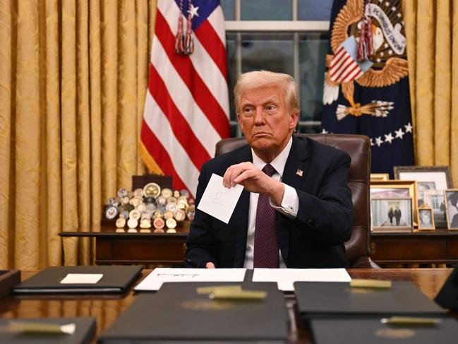 US President Donald Trump holds up outgoing President Joe Biden's letter as he signs executive orders in the Oval Office of the WHite House in Washington, DC, on January 20, 2025. (Photo by Jim WATSON / POOL / AFP)