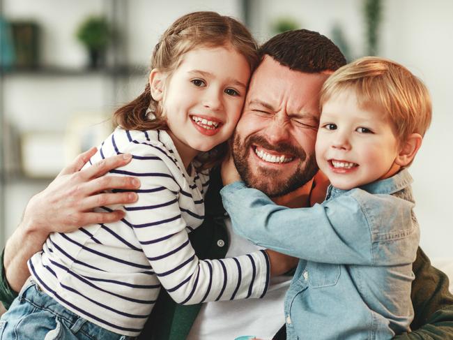 Adorable smiling little sister and brother hugging happy dad with gift box in hand while giving congratulations on fathers day at home