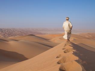 Man in traditional outfit in a desert at sunrise