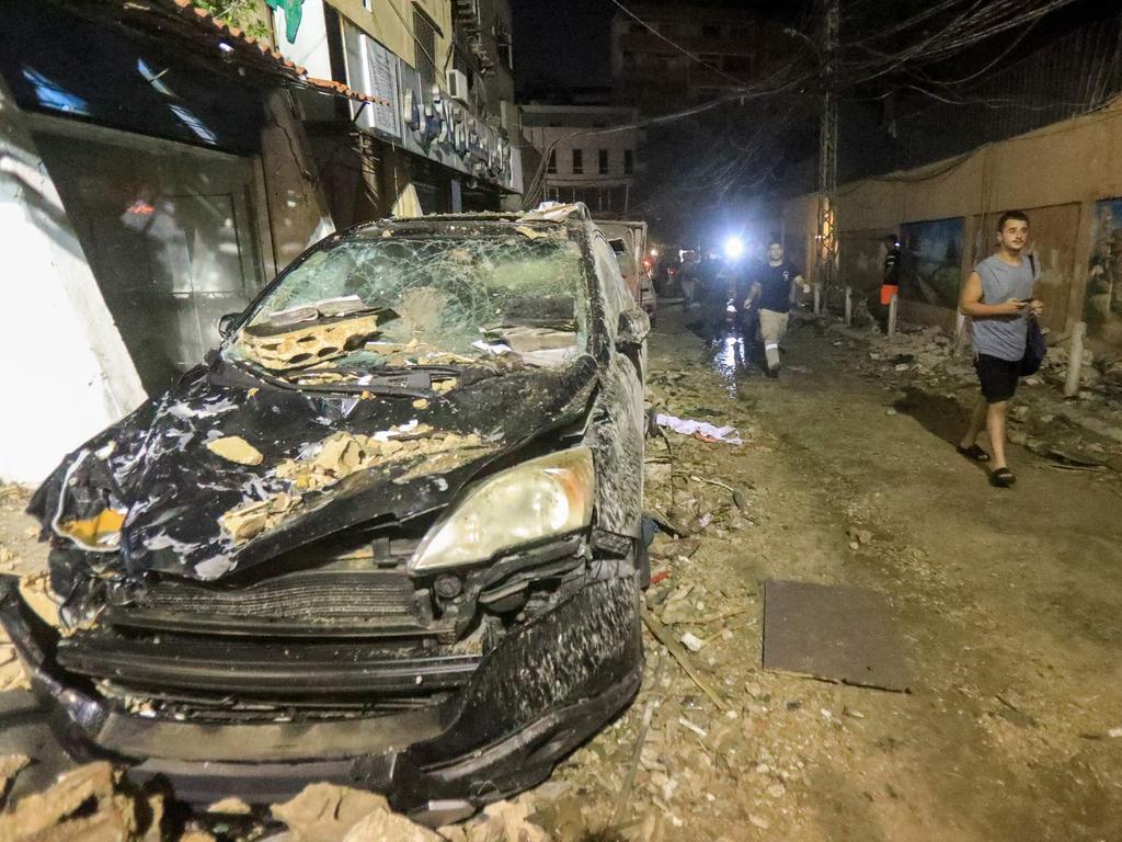 Men walk past debris and a destroyed car after the top floors of an eight-storey building. Picture: AFP