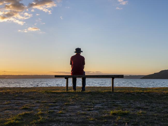 Man sitting alone by lake Rotorua at sunset, Mokoia Island in the distance, Rotorua. Picture: istock