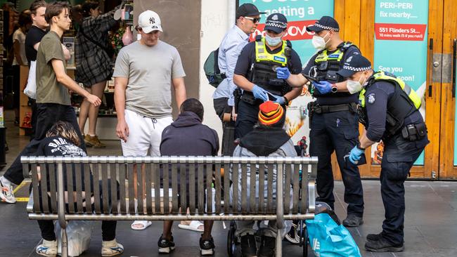 Officers question people sitting on a bench. Picture: Jake Nowakowski