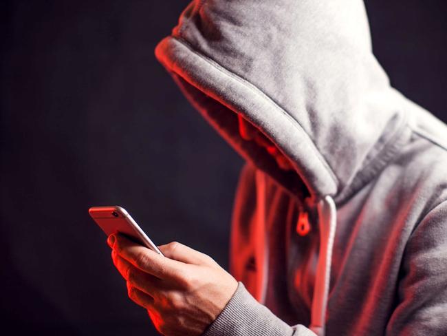 Man wearing hoody sweater with mobile phone in hands. Crime and hacking concept; scam generic.