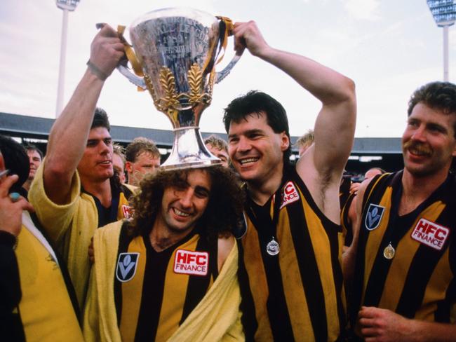 John Platten of the Hawks has the Premiership Cup propped on his head by team mates Gray Ayres (L), Chris Langford and Chris Mew looks on after the 1988 AFL Grand Final between the Hawthorn Hawks and the Melbourne Demons at the Melbopurne Cricket Ground.