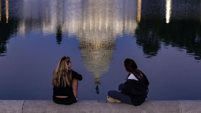 Two women sit on the edge of the Capitol Reflecting Pool, with the US Capitol building reflected in the water. Picture: Getty Images/AFP