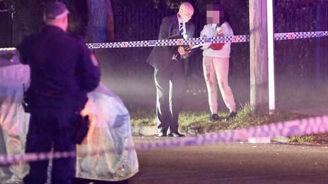 A woman covered in blood speaks with a detective at the crime last night. Picture: Steve Tyson