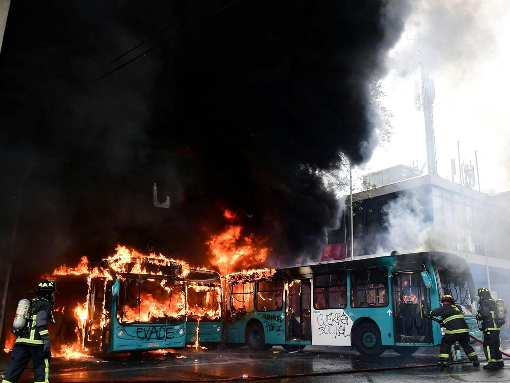 Chilean firefighters extinguish burning buses during clashes between protesters and the riot police in Santiago. Picture: AFP