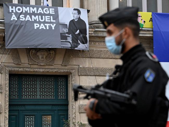 A French police officer stands next to a portrait of French teacher Samuel Paty on display on the facade of the Opera Comedie in Montpellier on October 21, 2020, during a national homage to the teacher who was beheaded for showing cartoons of the Prophet Mohamed in his civics class. - France pays tribute on October 21 to a history teacher beheaded for showing cartoons of the Prophet Mohamed in a lesson on free speech, an attack that has shocked the country and prompted a government crackdown on radical Islam. Seven people, including two schoolchildren, will appear before an anti-terror judge for a decision on criminal charges over the killing of 47-year-old history teacher Samuel Paty. (Photo by Pascal GUYOT / AFP)