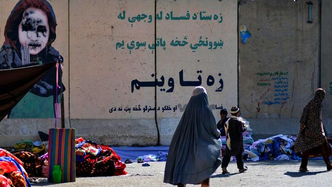 Women walk past a vendor selling second-hand clothes near a defaced mural at a market in Kandahar on September 22, 2021. Picture: Javed Tanveer/AFP