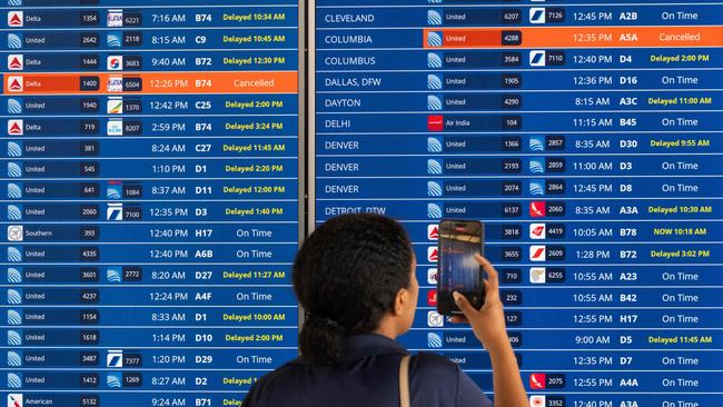 A woman uses the camera on her phone to record a flight information board showing multiple delays and some cancellations in flight departures from Dulles International Airport near Washington. Picture: Getty Images/AFP