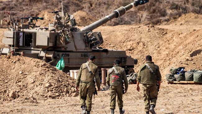 Israeli army soldiers walk near a self-propelled howitzer stationed near the border with Gaza in southern Israel.