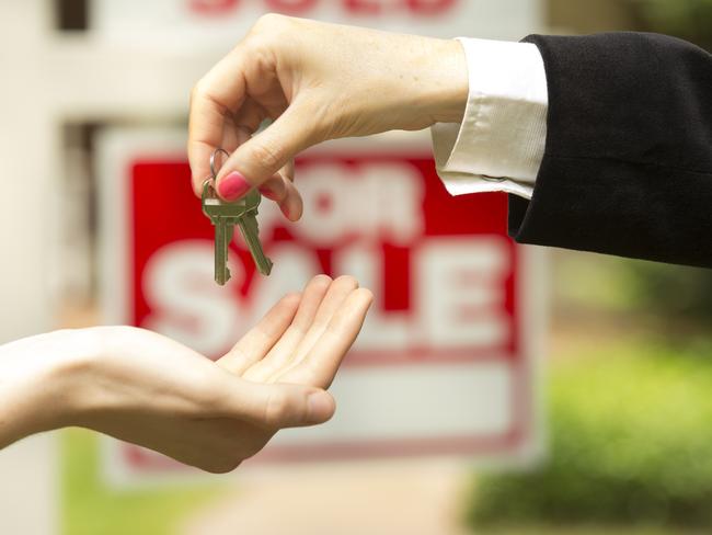 iStock photo of agent handing over keys in front of a for sale / sold sign. For On the Pulse column in Cairns Post weekend real estate liftout.