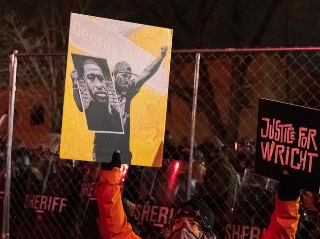 A demonstrator holding a poster of George Floyd and sign reading "Justice for Wright" in front of a line of police officers outside the Brooklyn Center police station while protesting the death of Daunte Wright who was shot and killed by a police officer in Brooklyn Center, Minnesota on April 14, 2021. - Minneapolis has been roiled by nights of violent protests after police officer Kim Potter, who is white, opened fire on Black 20-year-old Daunte Wrigh in his car on April 11. Potter, who shot dead Daunte Wright in a Minneapolis suburb after appearing to mistake her gun for her Taser, was arrested on April 14 and will face manslaughter charges. (Photo by Kerem Yucel / AFP)