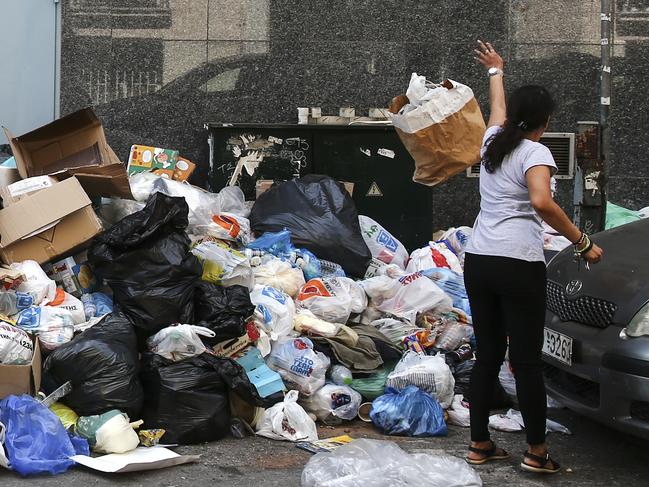 A woman throws a garbage bag onto a pile of garbage in Athens, on Thursday, June 29, 2017. A strike by garbage collectors, which has lasted nearly two weeks, has left towering mounds of garbage on city streets at a time when the summer's first heatwave sent temperatures soaring. (AP Photo/Yorgos Karahalis)