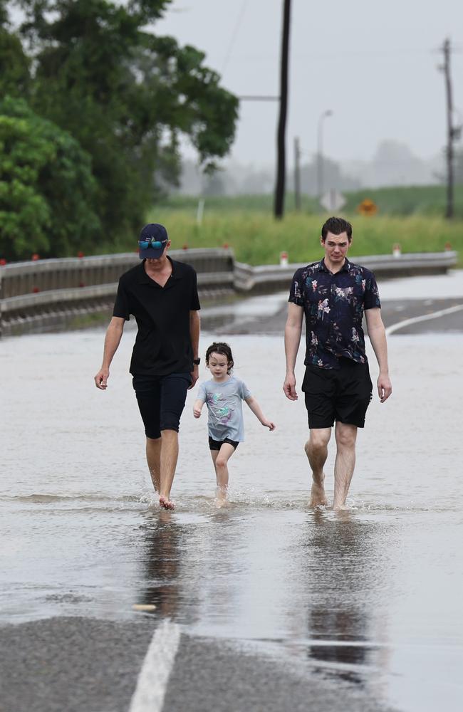 Robin Watson, Ella Watson, 5, and her father Leal Watson walk along the Bruce Highway after the road was cut off by flood water south of the Tully River at Euramo. Picture: Brendan Radke