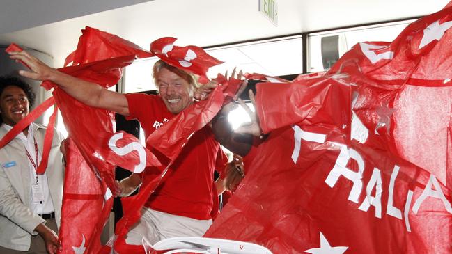 Richard Branson crashes through a ceremonial banner on the inaugural V Australia flight from Sydney to Los Angeles. Picture: Reed Saxon, AAP