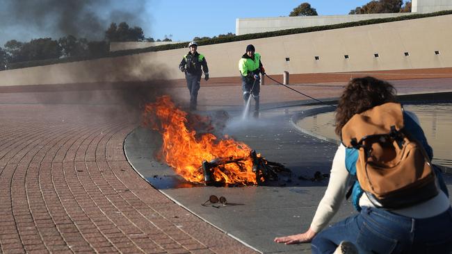 A policeman uses a fire extinguisher to put out a baby's pram that was on fire while a young female protester sits on the forecourt. Picture: NCA NewsWire / Gary Ramage