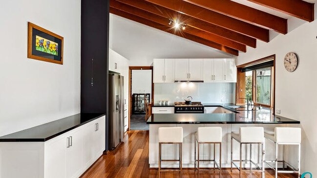 A vaulted ceiling with exposed timber beams, granite bench tops, soft closing drawers, white cabinetry, a Smeg oven, Bosch dishwasher and breakfast bar feature in the kitchen.