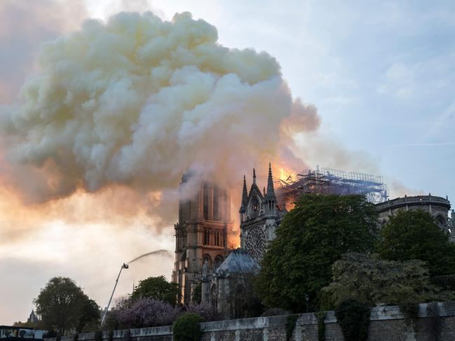 Flames and smoke are seen billowing from the roof at Notre-Dame Cathedral in Paris on April 15, 2019. - A huge fire swept through the roof of the famed Notre-Dame Cathedral in central Paris on April 15, 2019, sending flames and huge clouds of grey smoke billowing into the sky. The flames and smoke plumed from the spire and roof of the gothic cathedral, visited by millions of people a year. A spokesman for the cathedral told AFP that the wooden structure supporting the roof was being gutted by the blaze. (Photo by THOMAS SAMSON / AFP)