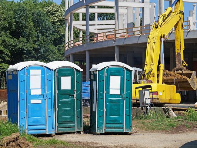 Mobile toilets at the construction site next to an excavator.