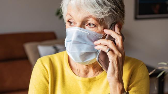 Photo of woman wearing a protective face mask at home and talking on the phone