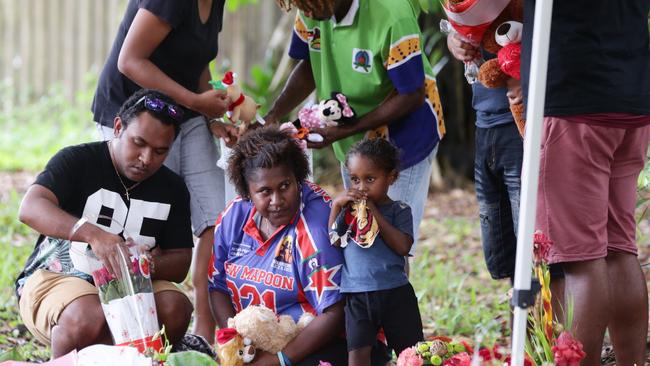 Lewis Warria (hat) and Norena Warria (sitting in middle) the surviving children of the Murray Street murder that claimed eight of their relatives lives, laying flowers and gifts at a memorial in Murray Street Park, Cairns. Photographer: Liam Kidston.