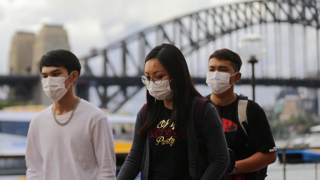 People wear face masks in front of the Sydney Harbour Bridge in Sydney, Monday, March 9, 2020. Picture: Steven Saphore