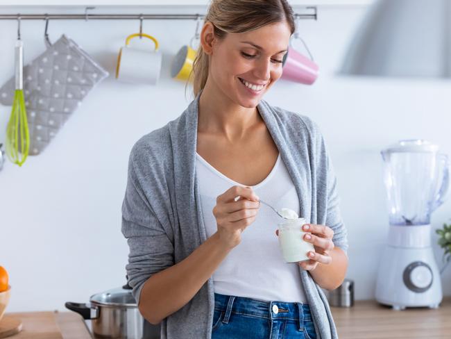 Shot of pretty young woman eating yogurt while standing in the kitchen at home.