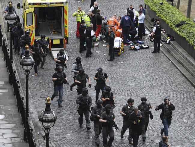 Armed police walk past emergency services attending to injured people on the floor outside the Houses of Parliament in London. Picture: Stefan Rousseau/PA via AP