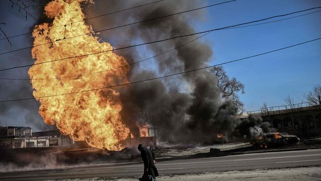 A Ukrainian woman walks past flames and smoke rising from a fire following an artillery fire, which Russia has claimed was a successful “first phase” Picture: AFP.