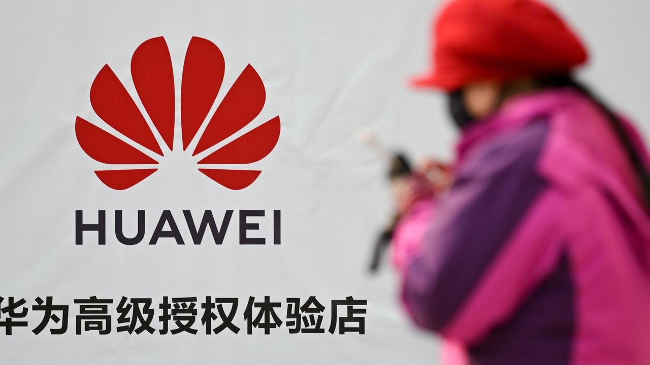 A woman uses her smartphone while walking past advertising outside a Huawei store in Beijing. Picture: AFP