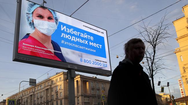 A man walks past an electronic billboard showing a doctor wearing a medical mask with the words reading “Avoid crowded places, it will save a life”", displayed in a street in St. Petersburg, Russia. Picture: AP