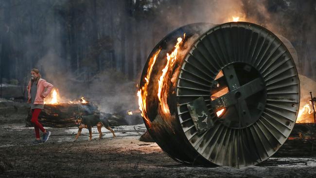 Jessica Tregellas walks her dog past a burning NBN cable spool. Picture: David Caird