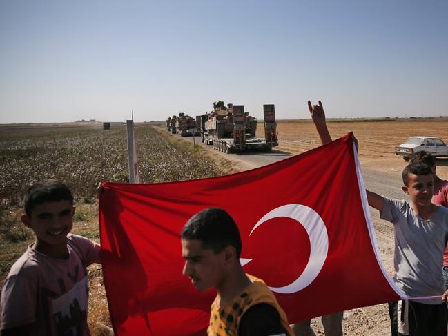 Local residents hold a Turkish flag as a convoy of Turkish forces trucks transporting tanks is driven in Sanliurfa province, southeastern Turkey, at the border with Syria. Picture: AP